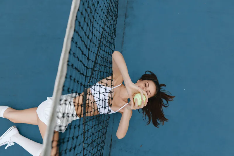 Happy young woman playing tennis on a blue court, wearing a sporty outfit and enjoying her game with a bright smile, perfect for sports and fitness themes