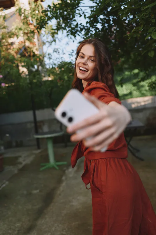 Smiling woman in a red dress takes a selfie outdoors, capturing a bright lifestyle moment with natural light and happy energy and carefree mood fills the frame