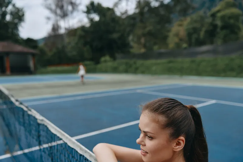 Athletic young woman enjoying a moment of contemplation on a tennis court, showcasing passion for healthy lifestyle and sports