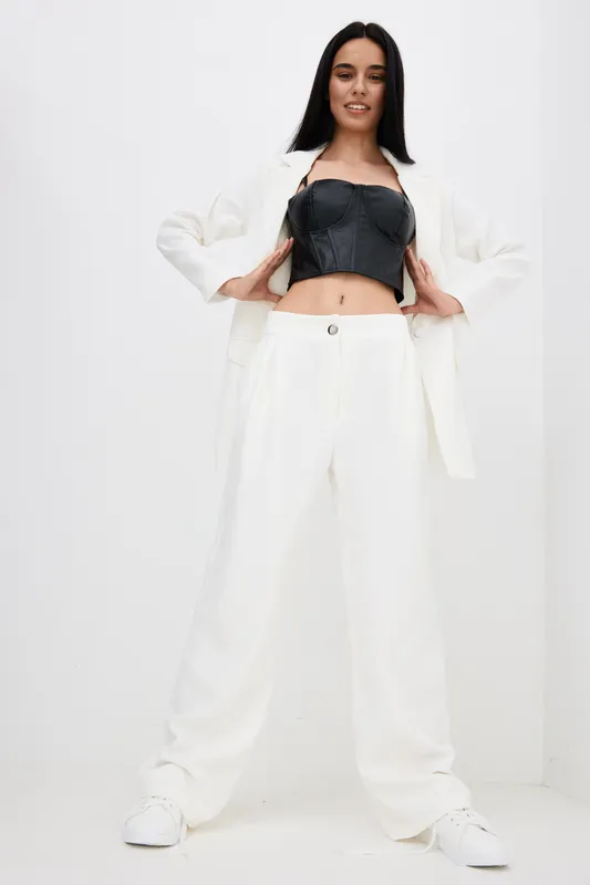 confident woman wearing white suit and black corset stands against white background with relaxed pose, casual style and modern fashion, studio portrait