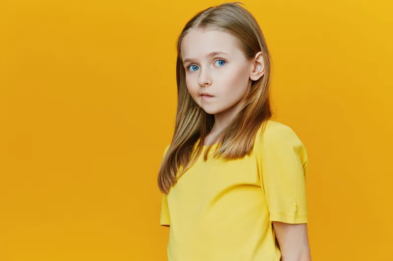 Young girl with long hair in a yellow t shirt against a vibrant yellow background, exuding a thoughtful emotion, perfect for seasonal or lifestyle themes