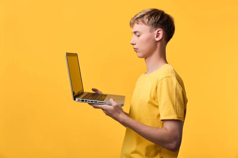 Youth with laptop in a yellow studio, showcasing technology, learning, and online education with a compact device for remote work and study in a bright minimalist setting