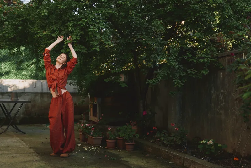 Woman in a red outfit stretches outdoors in a sunny garden, candid lifestyle moment, relaxed posture, sense of wellness and confidence, natural light and greenery