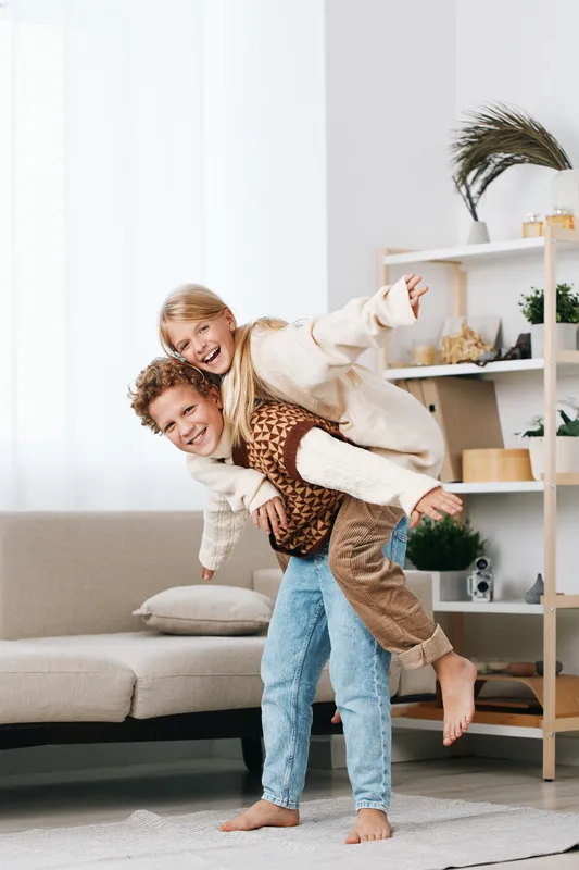 Authentic playful moment of children in a home setting, a piggyback ride that highlights lifestyle and school aged joy in a candid, uplifting scene.