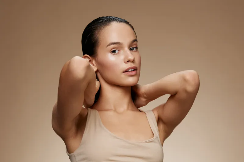 Young female model displaying healthy skin and natural beauty, posing with her hands in a minimalist setting, emphasizing skincare and self care