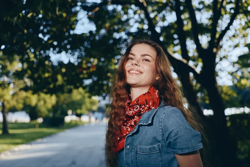 Lifestyle woman in modern boho-western denim street style smiling outdoors with film color effect and natural sunlight in a relaxed urban park setting.
