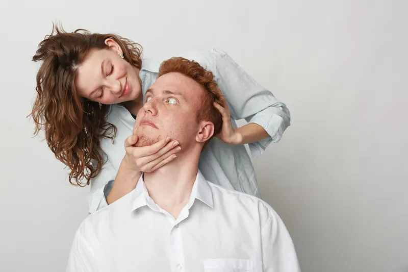 Young couple in casual clothes share intimate moment, woman gently holding man's face. White background, natural light, concept of love, affection, and relationship connection.