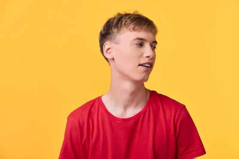 Young man, profile, red shirt, yellow background, studio shot, casual fashion, model, side view, masculine presence in bright setting and modern style for commercial use.