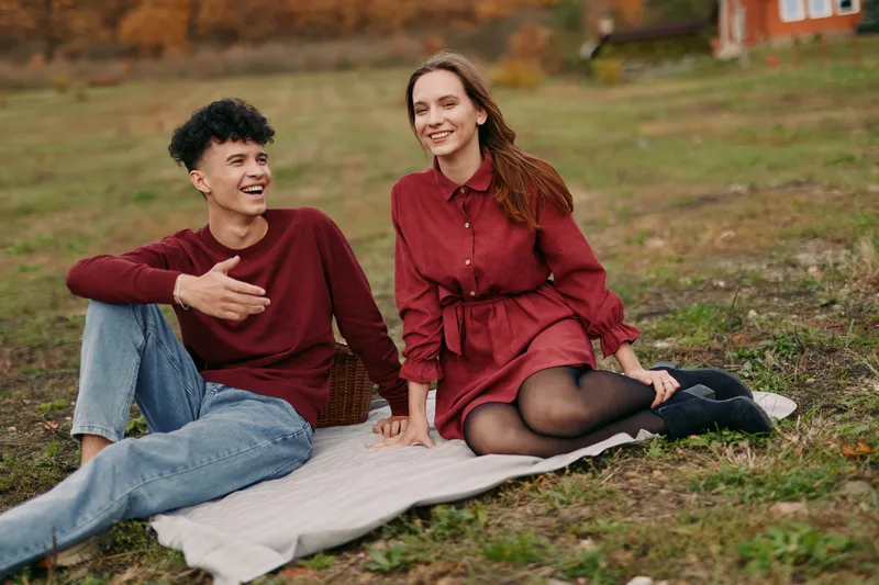 Young couple sharing a genuine outdoor moment on a blanket in autumn, captured with authenticity and credibility, natural expressions and relaxed body language conveying real connection.