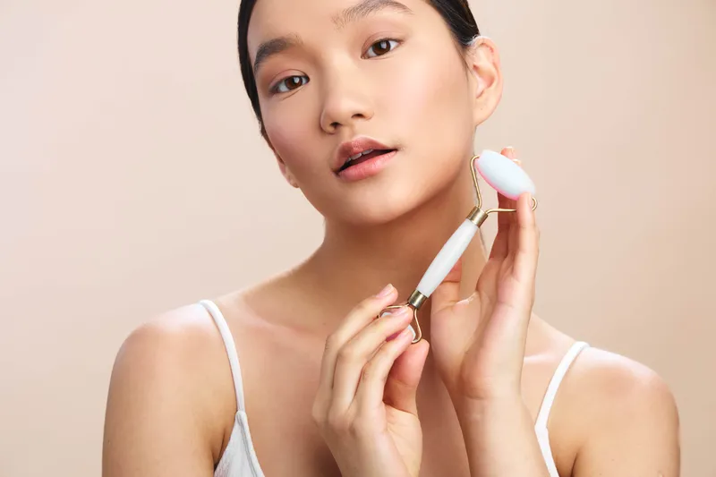 asian woman applies makeup with a soft brush in a calm studio setting, her expression poised and confident as light highlights her smooth skin and subtle makeup finish.