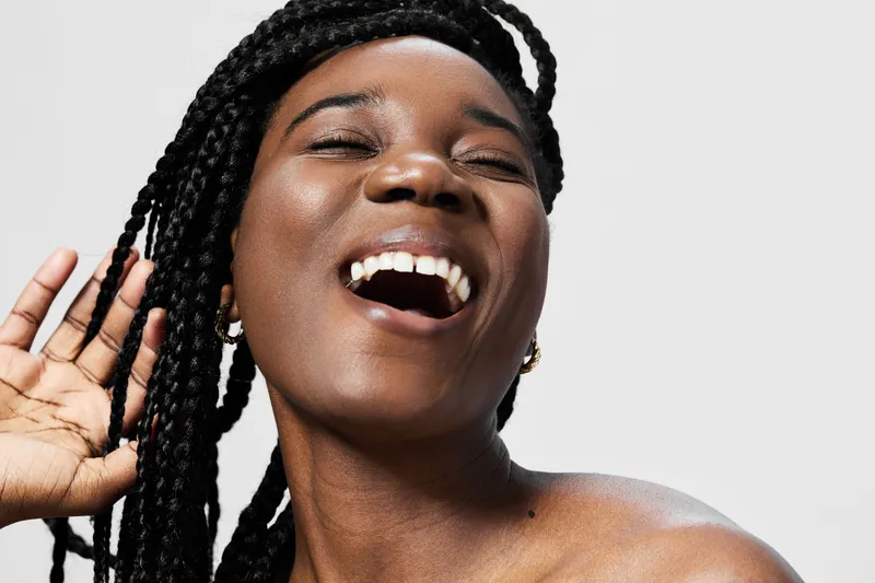 Cheerful African woman with braided hair smiling joyfully against a minimalist background, embodying happiness and confidence