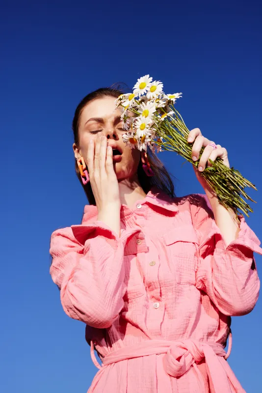 Young woman in a pink dress holds daisies against a clear blue sky, expressing joy and tranquility, embodying the essence of spring and emotional wellness