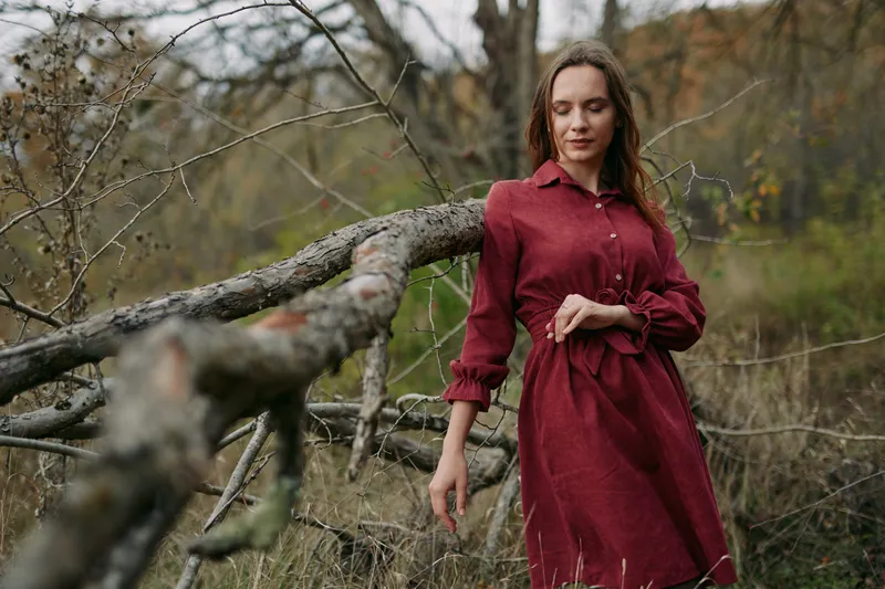 An authentic, candid portrait of a woman in a red dress moving through a wild field with weathered wood, capturing natural grace and honest, unposed mood.