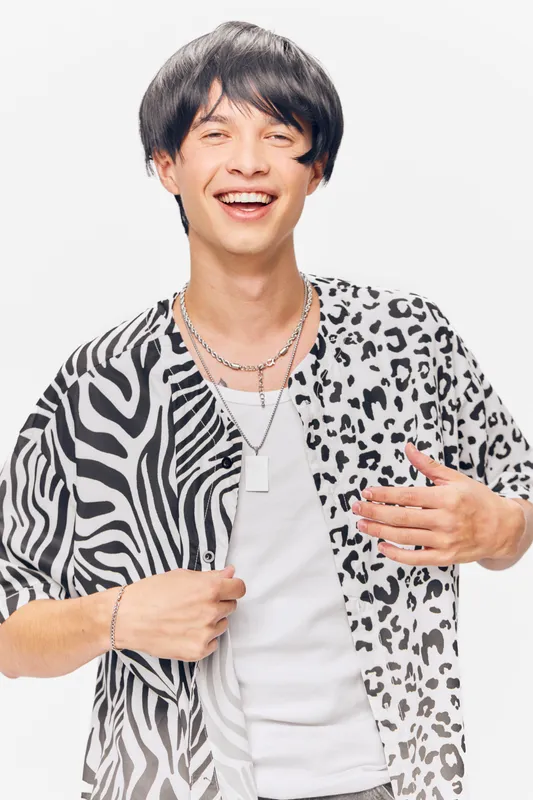 smiling young man wearing stylish black and white animal print shirt with layered necklaces, expressing happiness and casual fashion on white background
