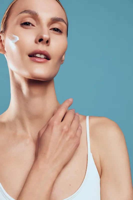Woman applying white face cream, closeup on blue background, skincare and beauty care, smooth skin and gentle touch, wellness mood with soft studio lighting
