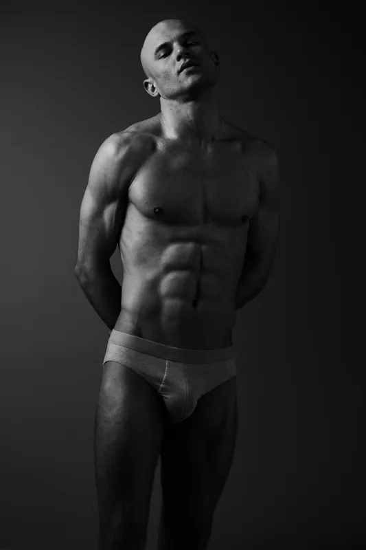 Strong man posing in a black and white image, showcasing impressive physique and confident expression. A striking portrayal of strength and masculinity in monochrome.