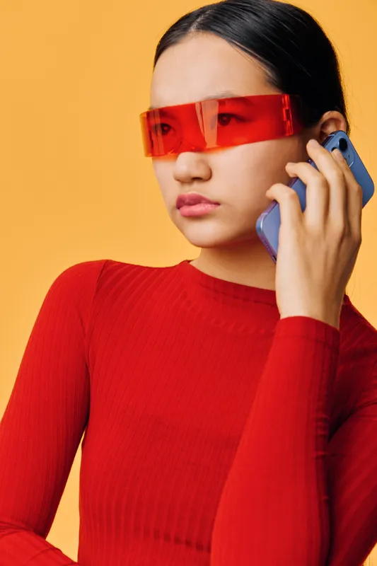 Woman wearing red sunglasses and red sweater using smartphone, communication and technology concept with vibrant yellow background for modern lifestyle and connectivity.