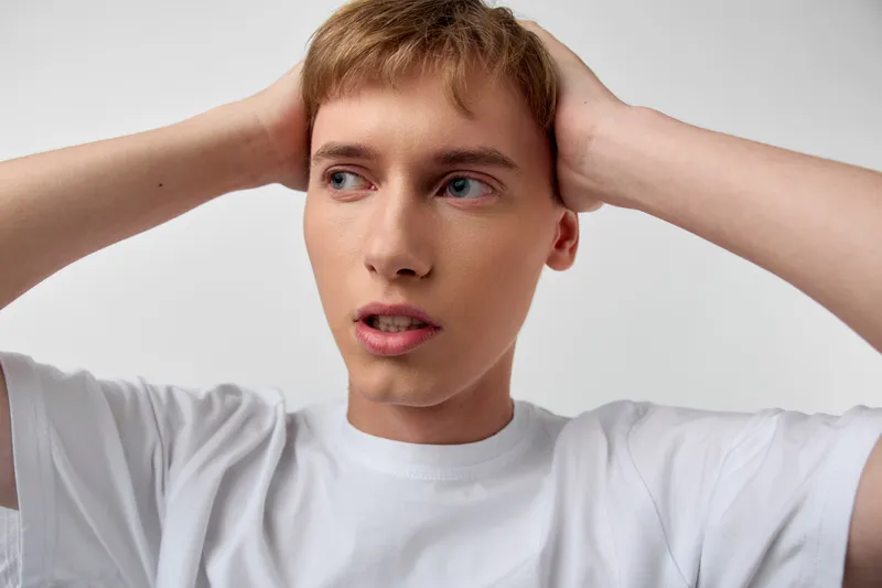 Man with hands on head, expressing confusion and stress, wearing a white t shirt. Close up shot highlights anxious mood, thoughtful gaze, and unsure posture suitable for themes of worry, mental