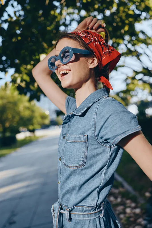 Lifestyle woman wearing modern boho-western denim street style with sunglasses and a red bandana, captured in vibrant film color outdoors, expressing joy and freedom.