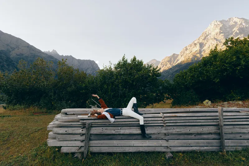 Person woman lying on logs in meadow, mountains and forest background, nature relaxation and outdoors resting pose during travel or escape, peaceful countryside scene with greenery