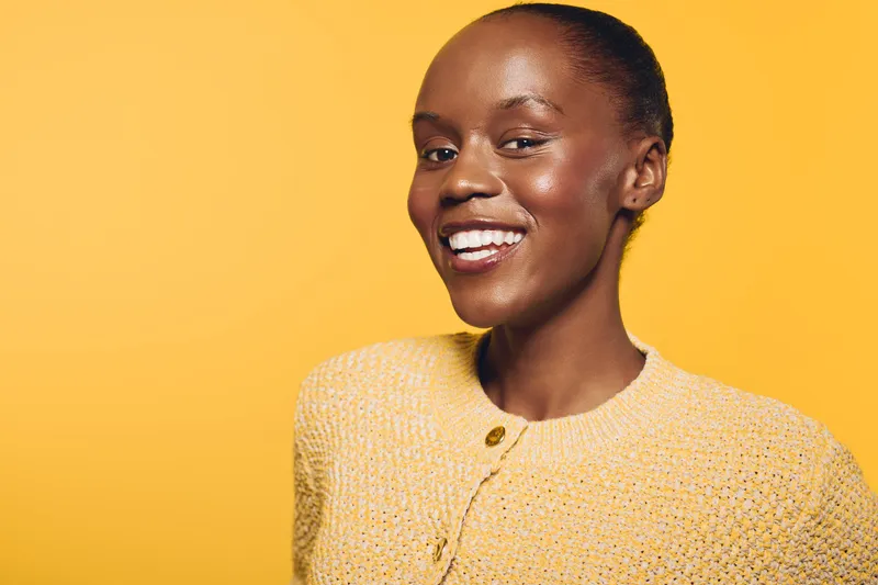 Smiling dark skinned African woman with short hair poses in yellow knitted sweater on yellow background. Concept of beauty, happiness, fashion, and natural skin care.