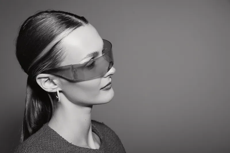 Profile of a fair skinned Caucasian woman wearing protective goggles and a grey sweater on grey background. Concept of safety and modern style.
