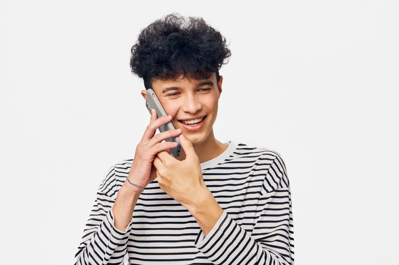 smiling teenage boy talking on phone, wearing striped shirt, curly hair, isolated on white background, casual and happy expression