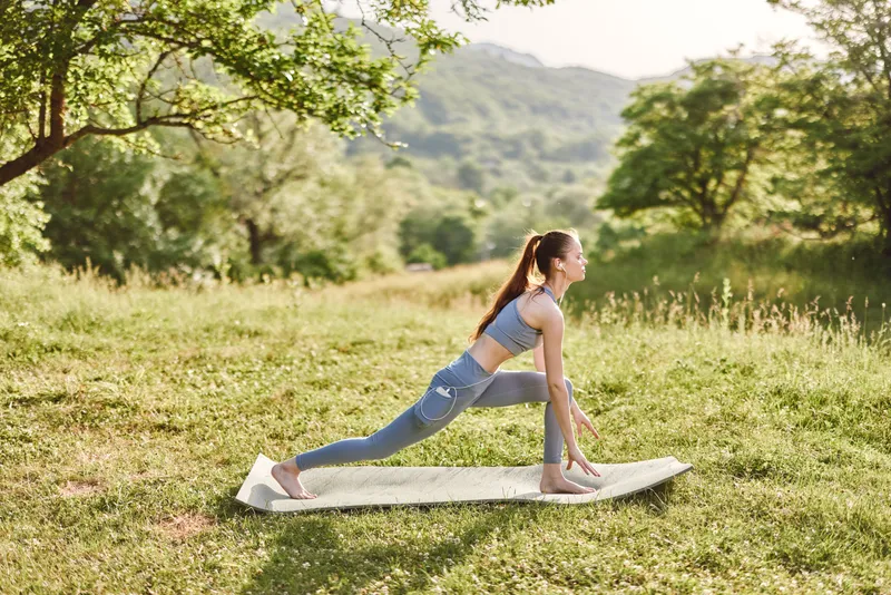 Young woman practicing yoga outdoors in a serene natural environment, showcasing flexibility and tranquility in athletic wear