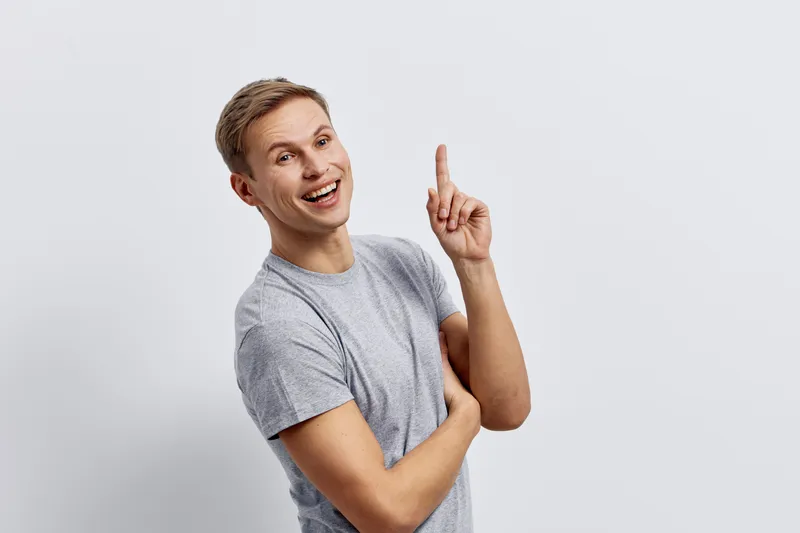 smiling man in gray t-shirt pointing finger up cheerful caucasian young adult casual pose isolated on light background concept digital nomad