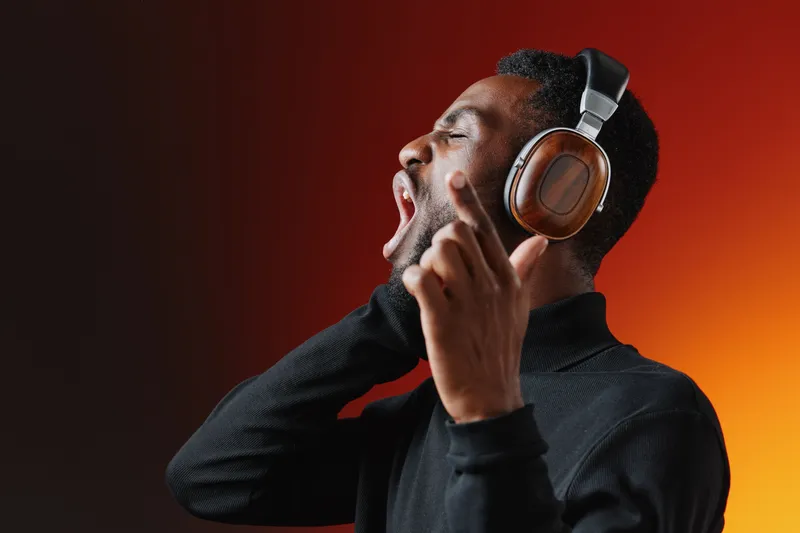A joyful Black man enjoying music in stylish headphones, with a vibrant orange and black gradient background, capturing emotions of happiness and passion for music