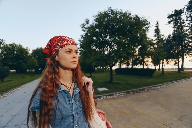 lifestyle woman in modern boho-western denim street style with a red bandana and natural makeup, captured in warm film color tones during golden hour outdoors