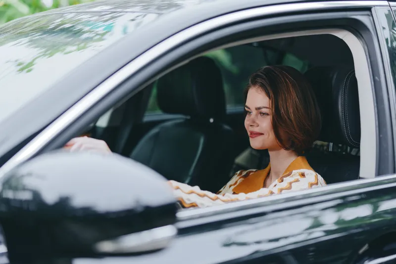 Portrait of a calm woman driving a car, hands on the wheel, focused gaze, and relaxed posture inside a contemporary vehicle.