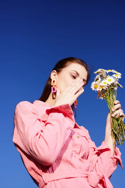 A young woman in a pink dress holding a bouquet of daisies against a clear blue sky, expressing joy and connection with nature, ideal for spring themed projects