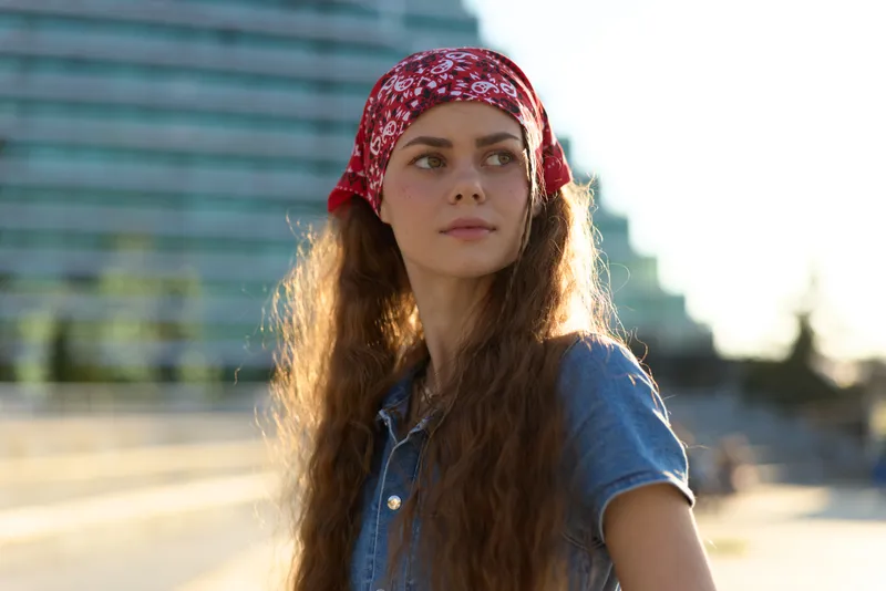 Lifestyle woman in modern boho-western denim street style with a red bandana, natural sunlight, and film color tones creating a warm and casual atmosphere.
