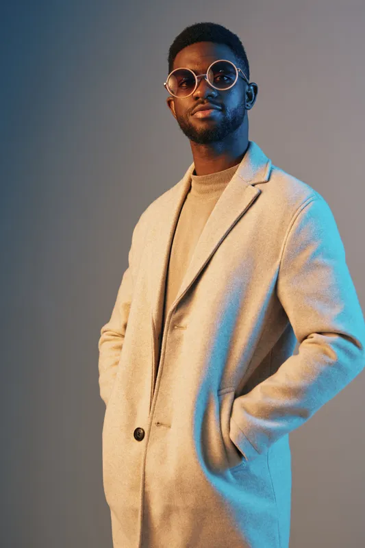 Stylish young man in a fashionable coat, showcasing modern fashion trends with confidence against a gradient background, ideal for fashion and lifestyle themes