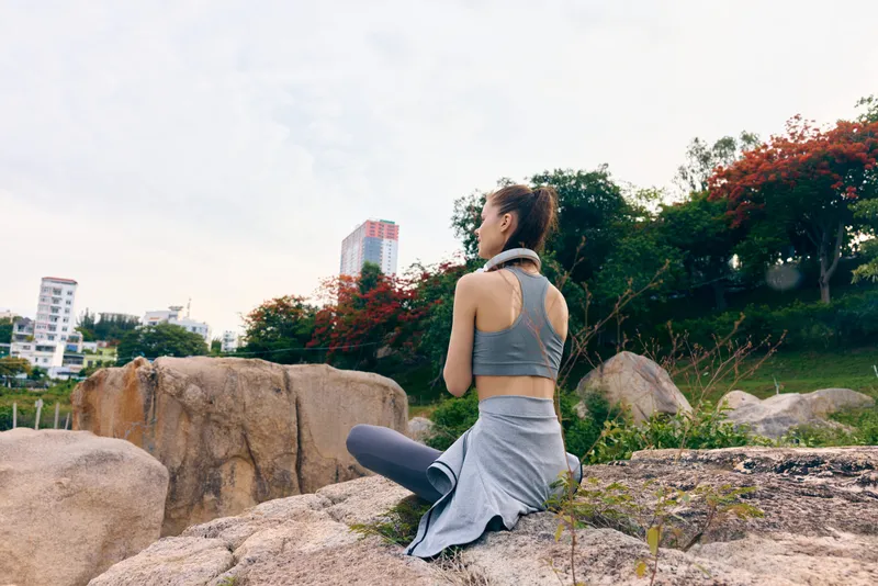 Young Asian woman practicing yoga outdoors, wearing comfortable activewear, surrounded by nature and rocks, conveying tranquility and mindfulness