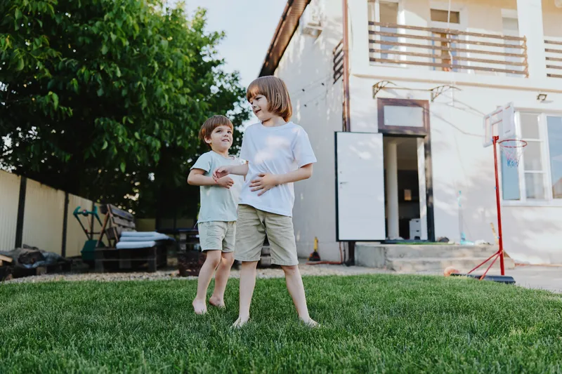Two happy children playing outdoors on green grass, enjoying a sunny day in a backyard. Their laughter fills the air, creating blissful memories of childhood fun. ###