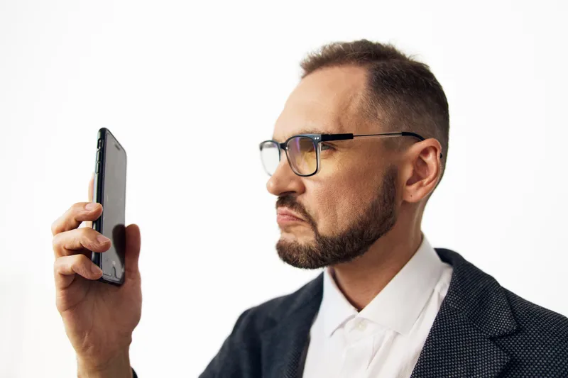 A focused business professional stands against a clean colored background, holding a smartphone to assess a message. His expression shows concentration and confidence, capturing a moment of strategic