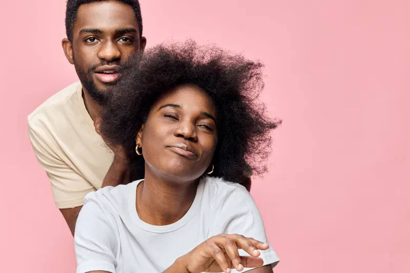 Portrait of a joyful couple with natural hairstyles, embracing each other against a pink background, expressing love and happiness in a vibrant setting