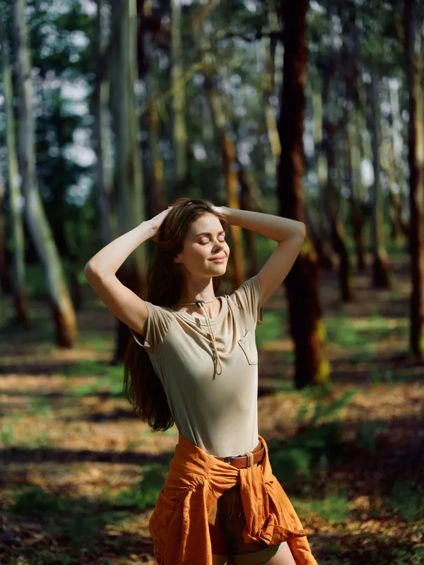 woman forest sunlight relaxation nature portrait longhair outdoors enjoying a peaceful moment with closed eyes and gentle smile, casual shirt and tied jacket around waist in warm woodland