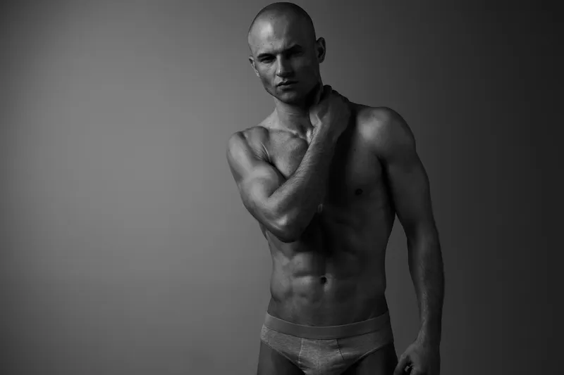 Black and white portrait of a muscular man expressing confidence and strength, showcasing his well-defined physique and powerful presence.