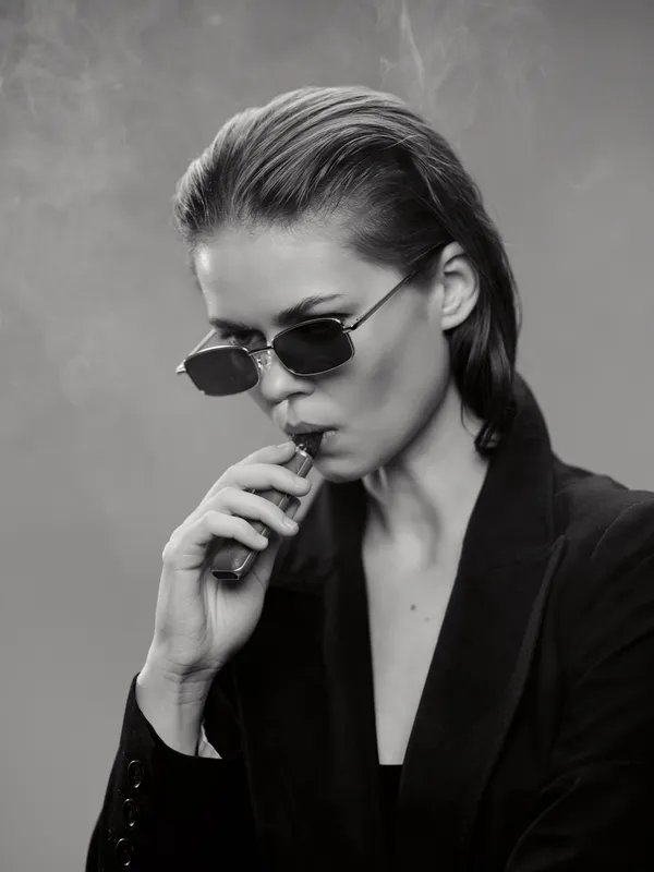 stylish woman vaping in black coat with sunglasses in black and white artistic portrait