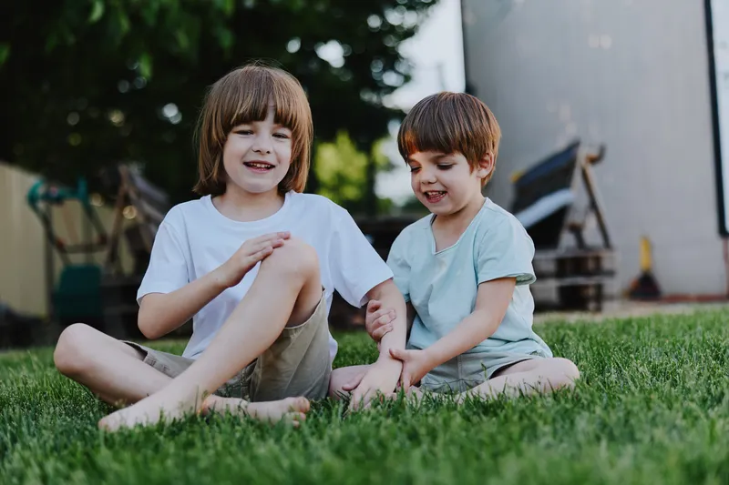 Two joyful boys playing outdoors in a sunny garden, sharing laughter and fun moments on the grass. Their happiness reflects a carefree childhood experience.