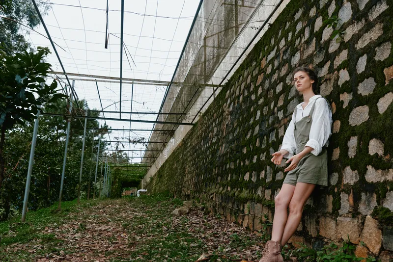 Young woman in casual outfit expressing emotions outdoors against a textured stone wall, showcasing a connection with nature and tranquility