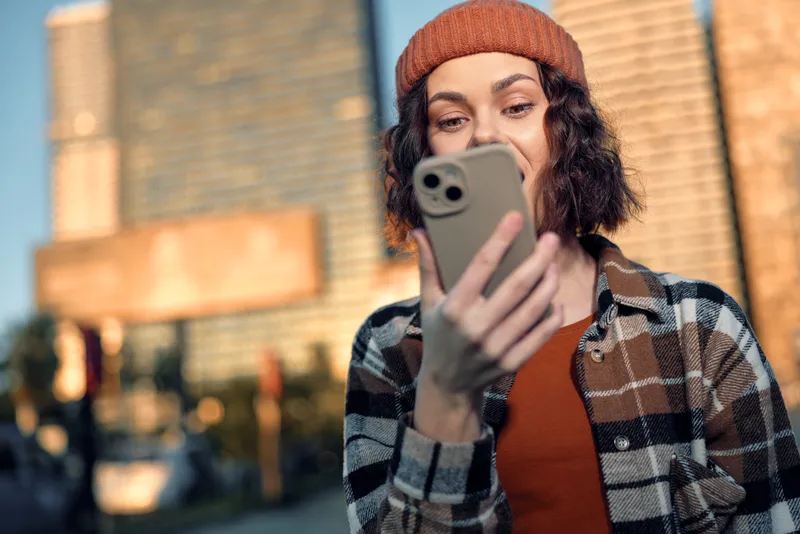 woman smartphone urban portrait candid beanie smile golden authentic candid lifestyle scene with golden hour glow, emotional storytelling and mindful living as young woman texts in warm city light.