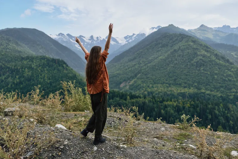 woman mountains hiking nature outdoors landscape on ridge arms raised at summit, authentic inclusive solo traveler enjoying wilderness freedom scenic view