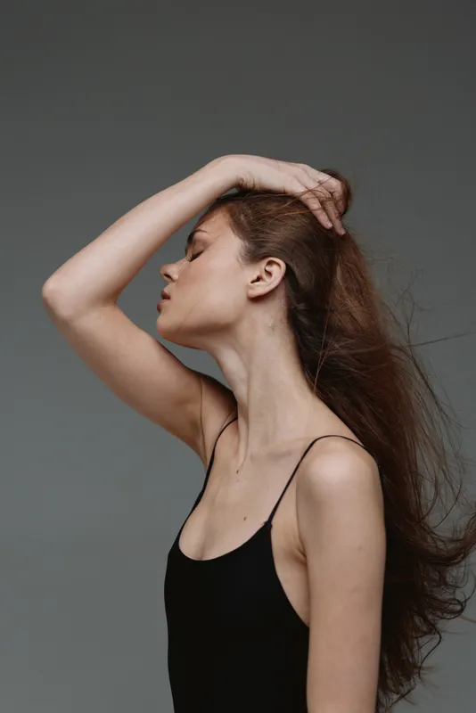 Profile of a young woman with flowing hair in black top against gray background, showcasing elegance and calmness.