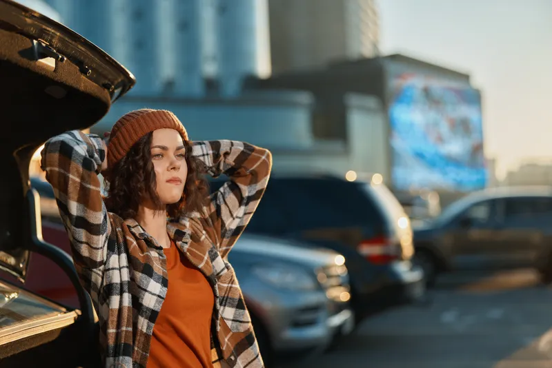 Woman by car in urban parking, authenticity and candid lifestyle moment during golden hour glow. Thoughtful portrait, mindful living and emotional storytelling in contemporary city scene