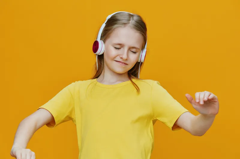 Happy girl enjoying music with headphones against a vibrant yellow background, showcasing joy and youthful spirit, perfect for music or lifestyle themes