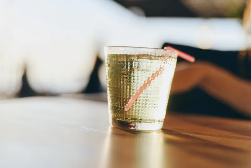 sparkling glass with clear water and a pink straw on wooden surface with blurred background in warm light, refreshing drink concept